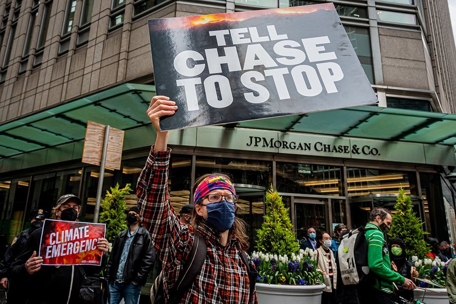 climate activists protest outside jpmorgan chase hq with signs that read "tell chase to stop" and "climate emergency"