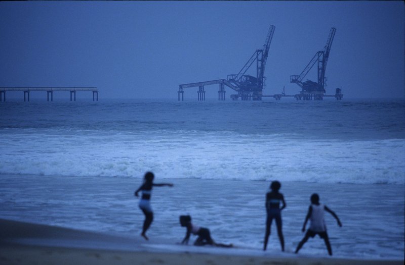 children play on Congo beach with oil rig in background at sea