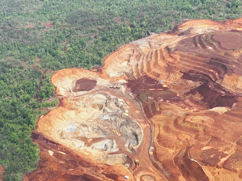 Trucks and diggers look tiny in a muddy deforested area on Gag island caused by nickel mining