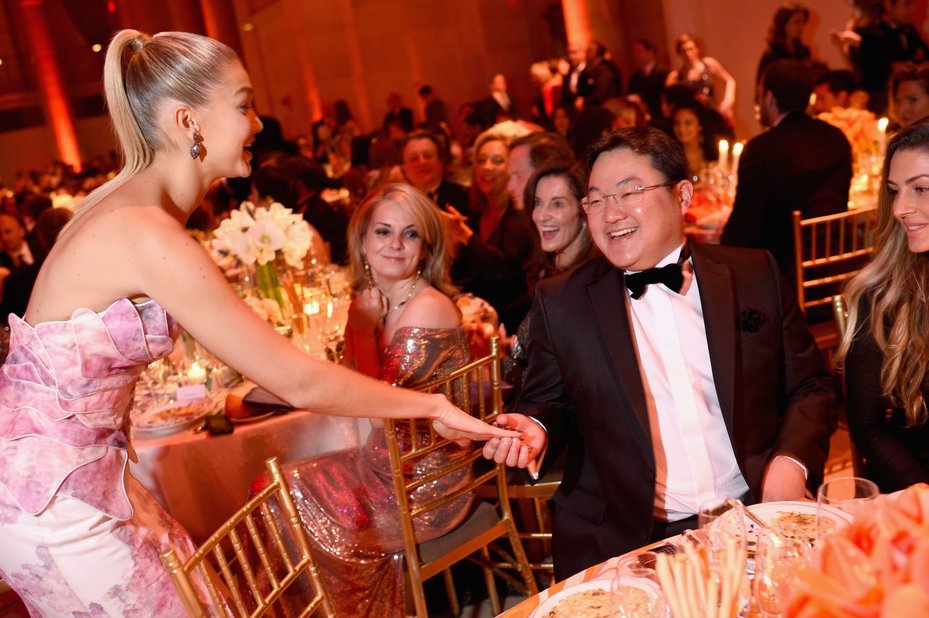 Jho low sitting at table at new york party while woman in pink dress talks to him