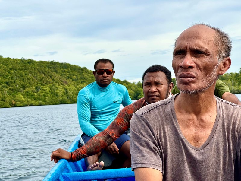 Community members on a boat looking at a sacred beach under threat from nickel mining