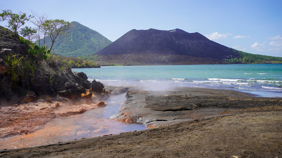 view of beach and ocean with Mount Tarvurvur Volcano in background in Rabaul, East New Britain, Papua New Guinea.