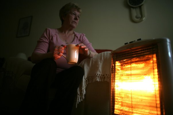 A pensioner keeps warm with the aid of an electric heater