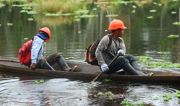 two OSINFOR inspectors float down the river on boat in Peru forest