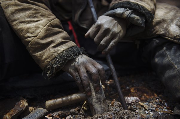 An artisanal miner holds his sledgehammer and a piece of rebar