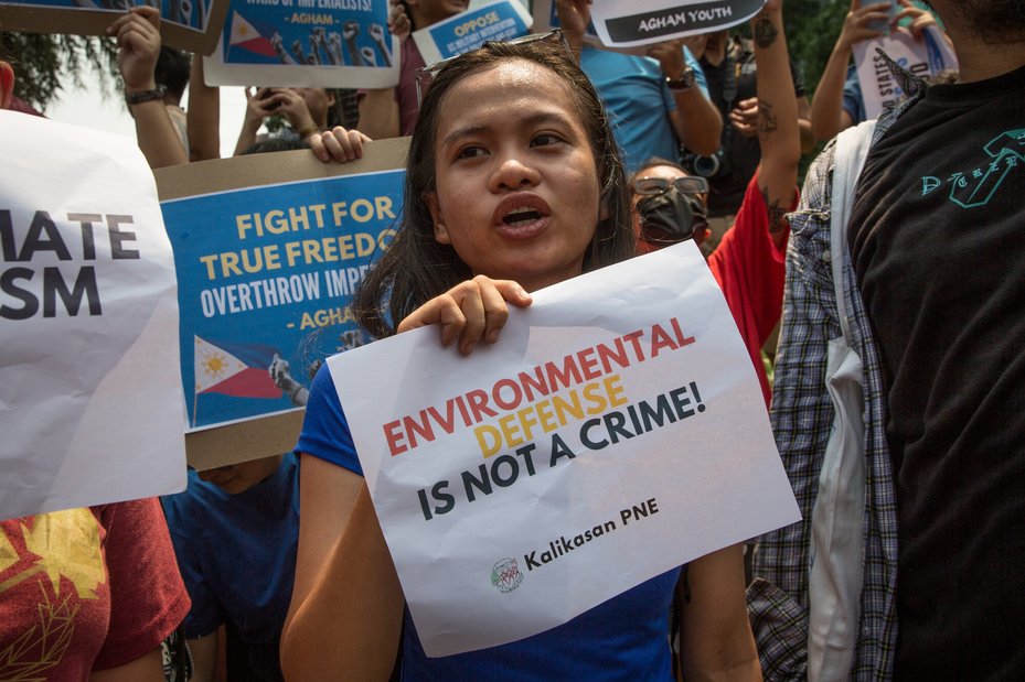 environmental defender Jonila Castro holds up sign saying "environmental defense is not a crime!" at a protest in The Philippines