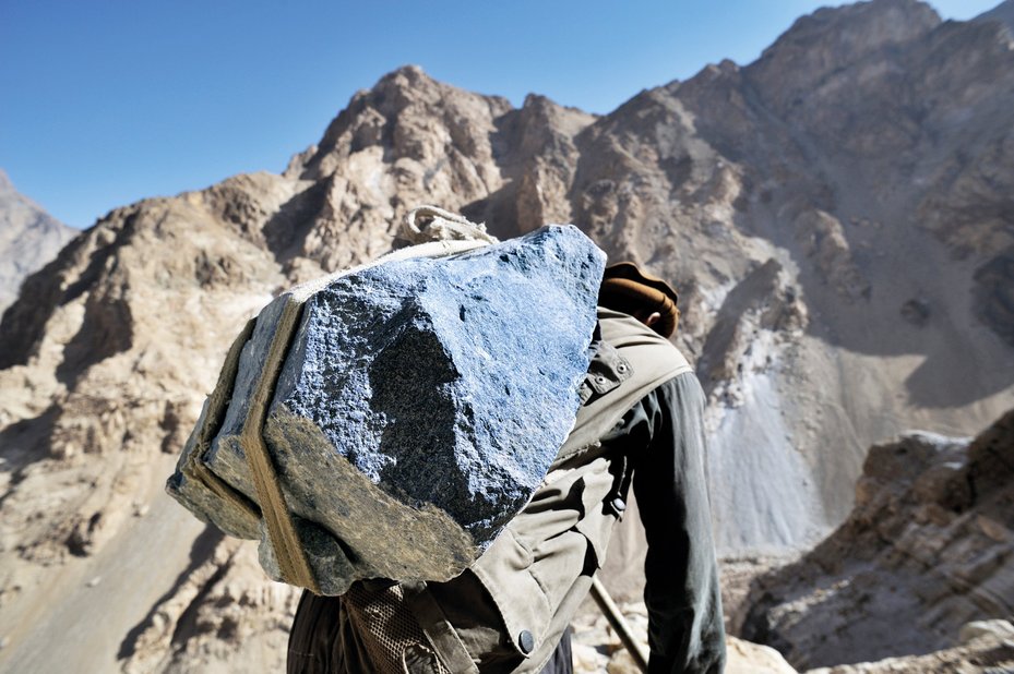 A worker at a lapis lazuli mine carries a back-breaking load of lapis down to the valley