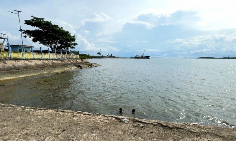 View over murky water with two children in the water and ship on horizon in distance